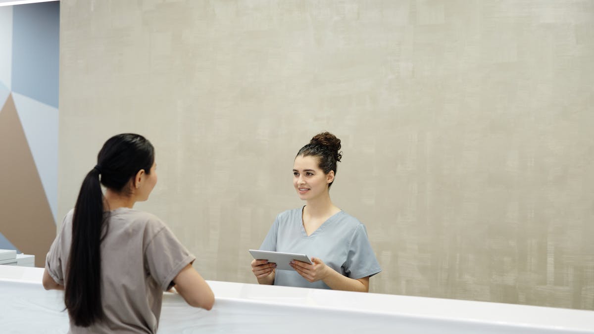 A medical receptionist with a tablet helping a patient at the front desk
